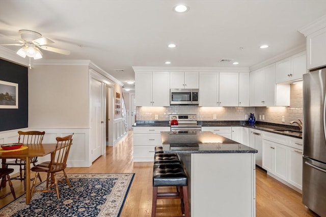 kitchen featuring stainless steel appliances, white cabinets, a sink, a kitchen island, and light wood-type flooring