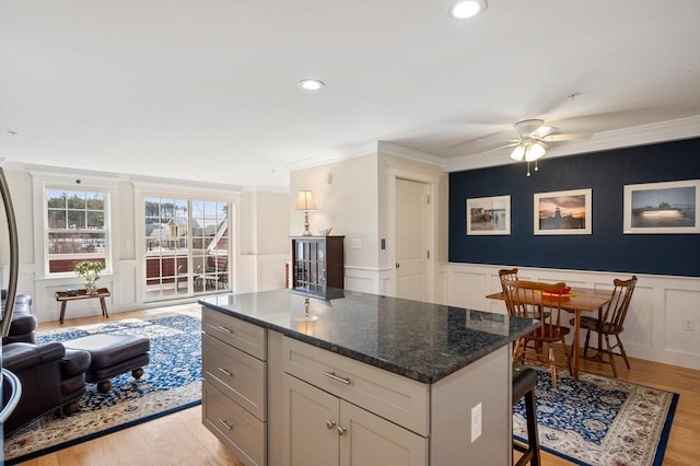 kitchen featuring ornamental molding, light wood-style floors, wainscoting, and a center island