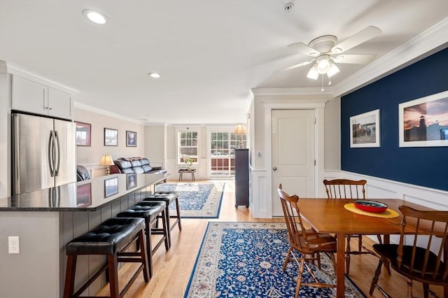 interior space featuring ornamental molding, freestanding refrigerator, light wood-style floors, wainscoting, and a kitchen bar