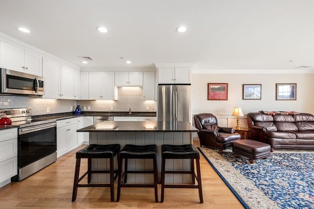 kitchen featuring stainless steel appliances, a breakfast bar, open floor plan, dark countertops, and crown molding