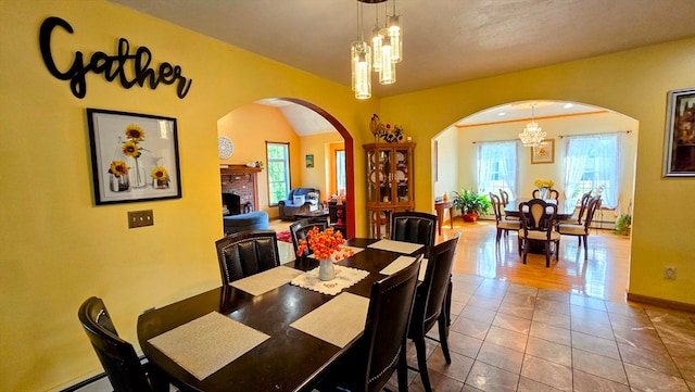 tiled dining space with a baseboard heating unit, a brick fireplace, and a notable chandelier