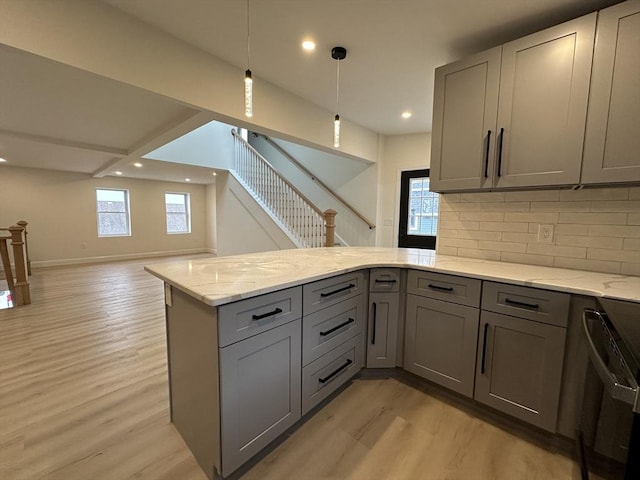 kitchen with hanging light fixtures, light hardwood / wood-style flooring, gray cabinets, kitchen peninsula, and backsplash