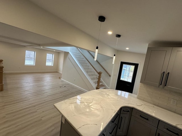 kitchen featuring gray cabinets, light stone countertops, a healthy amount of sunlight, and pendant lighting