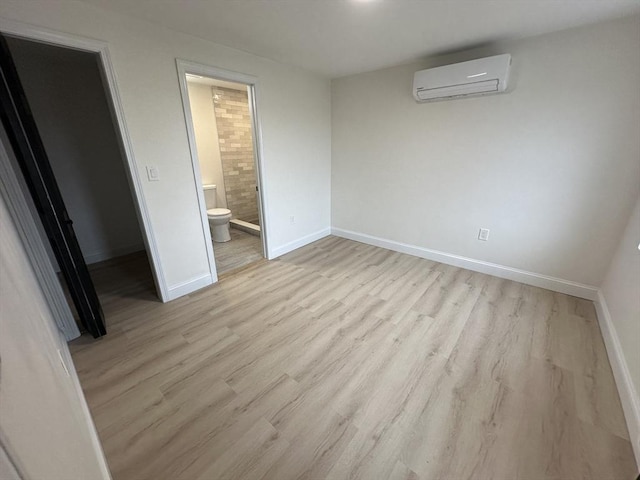 unfurnished bedroom with an AC wall unit, light hardwood / wood-style floors, and ensuite bath