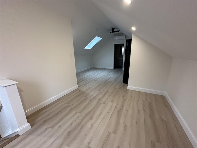 bonus room with a wall mounted air conditioner, lofted ceiling with skylight, light hardwood / wood-style floors, and ceiling fan