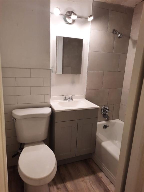 full bathroom with tiled shower / bath, wood-type flooring, tile walls, vanity, and toilet