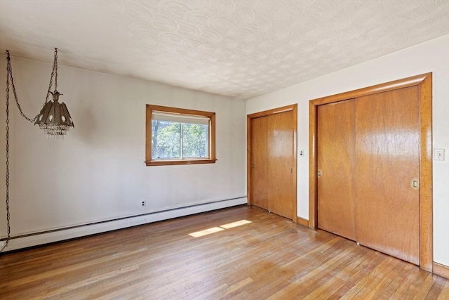 unfurnished bedroom with a baseboard radiator, multiple closets, light wood-style flooring, and a textured ceiling