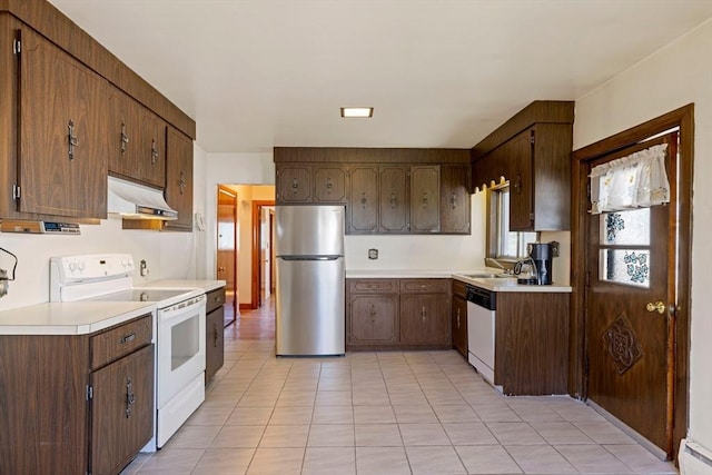 kitchen featuring light tile patterned floors, a sink, light countertops, under cabinet range hood, and white appliances