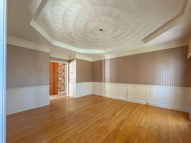 unfurnished room with a tray ceiling, a wainscoted wall, a decorative wall, and wood finished floors