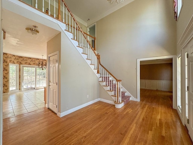 stairway featuring wood finished floors, ornamental molding, baseboards, a high ceiling, and a notable chandelier