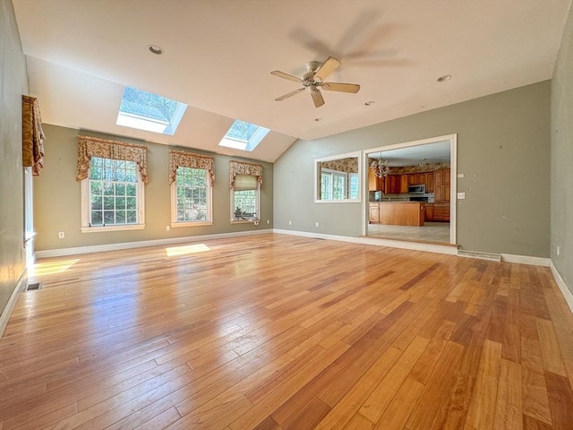 unfurnished living room with vaulted ceiling with skylight, light wood finished floors, a ceiling fan, and a healthy amount of sunlight