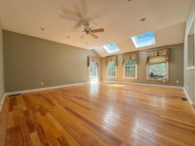 unfurnished room featuring baseboards, lofted ceiling with skylight, visible vents, ceiling fan, and light wood-style floors