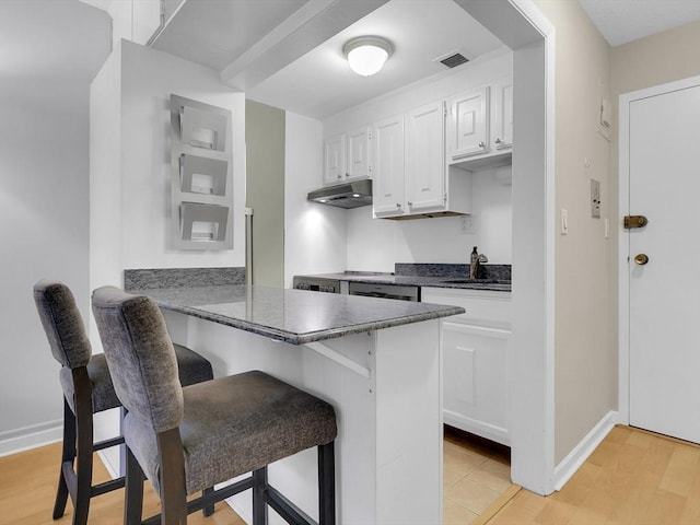 kitchen featuring white cabinets, sink, kitchen peninsula, light wood-type flooring, and a breakfast bar