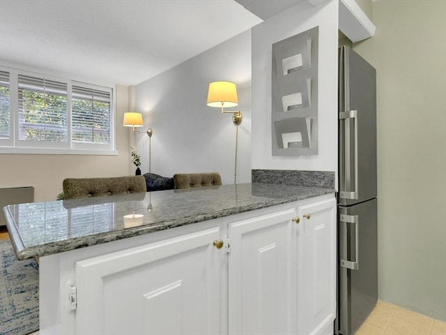 kitchen with white cabinetry, dark stone countertops, kitchen peninsula, and stainless steel refrigerator