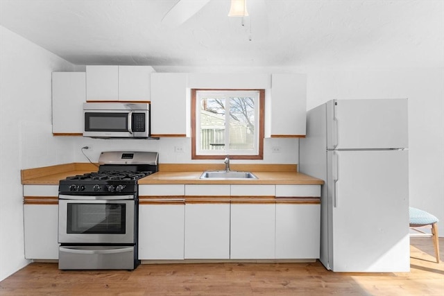 kitchen featuring stainless steel appliances, light countertops, white cabinetry, and a sink