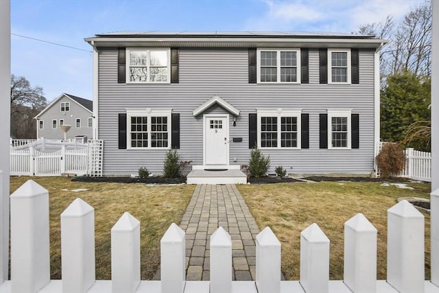 colonial inspired home with solar panels, a front lawn, fence, and a gate