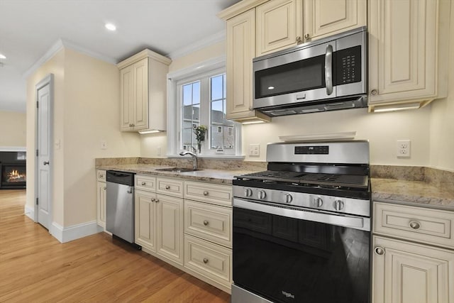 kitchen featuring appliances with stainless steel finishes, ornamental molding, cream cabinets, light wood-type flooring, and a sink