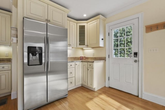 kitchen featuring light stone counters, cream cabinets, light wood-style floors, stainless steel fridge with ice dispenser, and glass insert cabinets