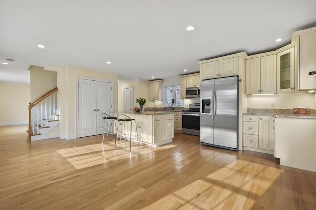 kitchen with cream cabinetry, a breakfast bar area, recessed lighting, appliances with stainless steel finishes, and light wood-style floors