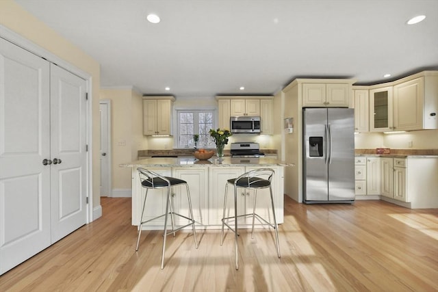 kitchen featuring appliances with stainless steel finishes, cream cabinetry, light wood finished floors, and light stone countertops