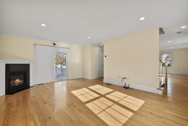 unfurnished living room featuring light wood-style flooring, recessed lighting, a fireplace with flush hearth, baseboards, and stairs