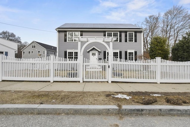 colonial house with a fenced front yard, a gate, and solar panels