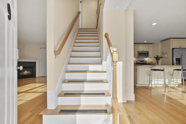 stairs featuring a glass covered fireplace, wood finished floors, and recessed lighting