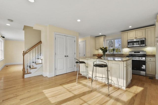 kitchen featuring light wood-style flooring, a breakfast bar area, appliances with stainless steel finishes, a center island, and cream cabinetry