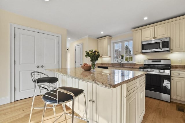 kitchen featuring stainless steel appliances, cream cabinetry, a kitchen island, and a sink