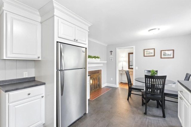 kitchen featuring freestanding refrigerator, dark countertops, white cabinetry, a brick fireplace, and ornamental molding