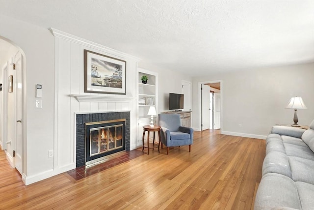 living area featuring arched walkways, light wood finished floors, a tiled fireplace, baseboards, and built in shelves