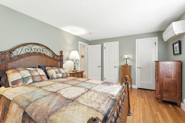 bedroom featuring an AC wall unit, light wood-style floors, baseboards, and a textured ceiling