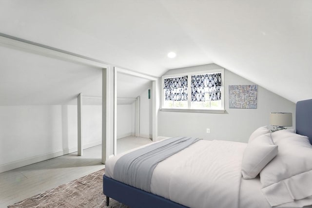 bedroom featuring wood finished floors, vaulted ceiling, multiple closets, and baseboards