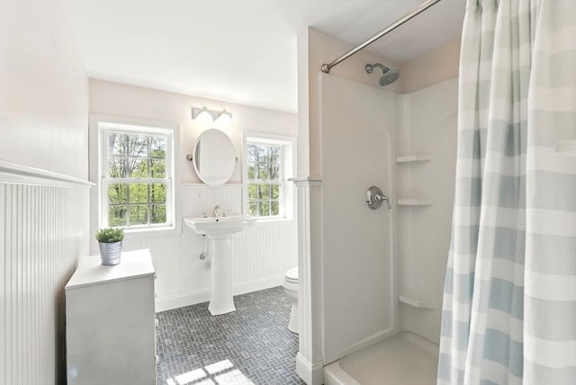 bathroom with a shower with shower curtain, wainscoting, plenty of natural light, and toilet