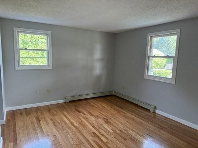 empty room with a baseboard heating unit, a textured ceiling, and light hardwood / wood-style floors