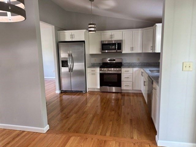 kitchen with appliances with stainless steel finishes, white cabinetry, wood-type flooring, and vaulted ceiling