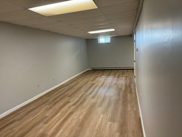 basement featuring baseboard heating, a drop ceiling, and wood-type flooring