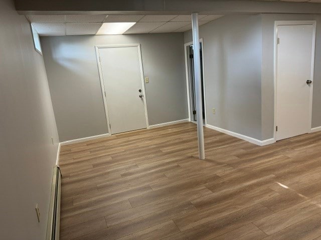 basement featuring a paneled ceiling, hardwood / wood-style flooring, and a baseboard radiator