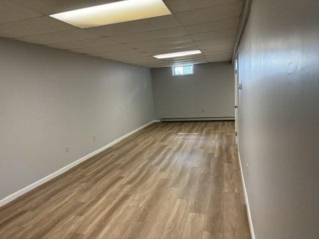 empty room with hardwood / wood-style flooring, a baseboard radiator, and a drop ceiling