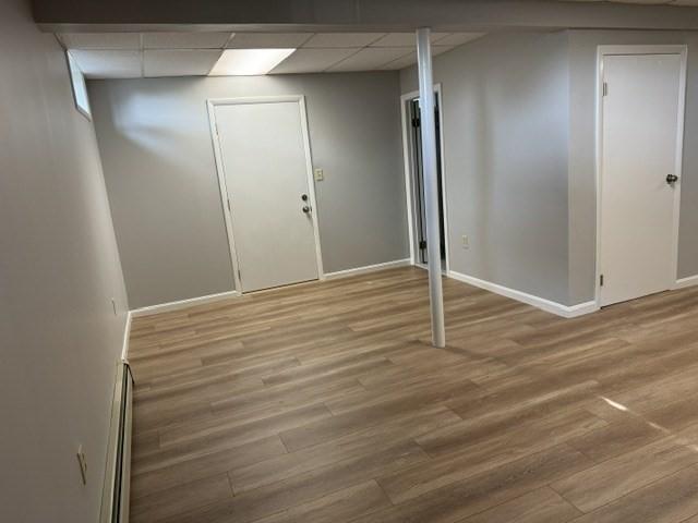 corridor with a drop ceiling, a baseboard heating unit, and light wood-type flooring