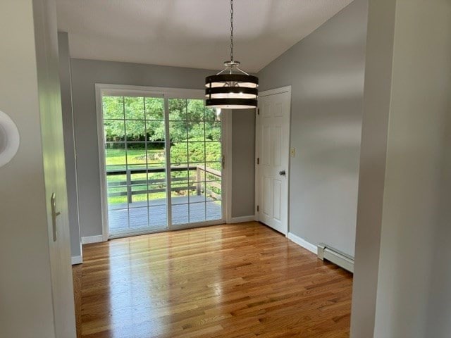 unfurnished dining area featuring vaulted ceiling, a baseboard radiator, and light wood-type flooring