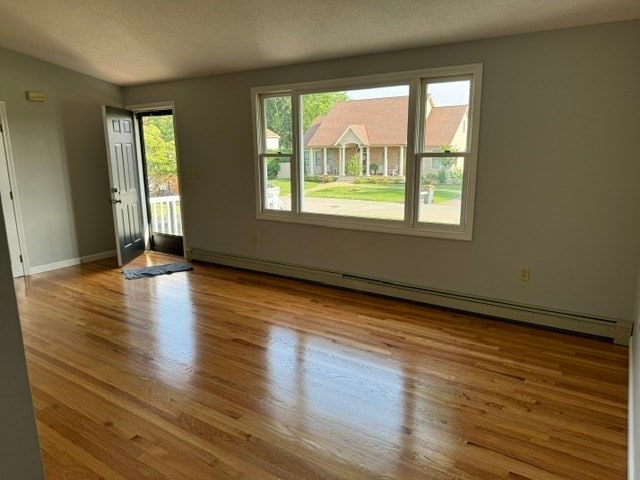 unfurnished room featuring a textured ceiling, a baseboard radiator, and light wood-type flooring