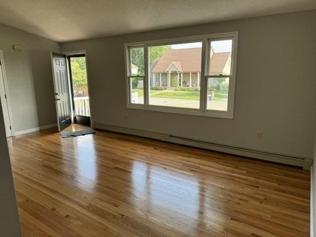 empty room with hardwood / wood-style floors, a baseboard radiator, and a healthy amount of sunlight