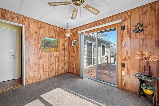 doorway to outside with wooden walls, baseboards, a drop ceiling, ceiling fan, and carpet