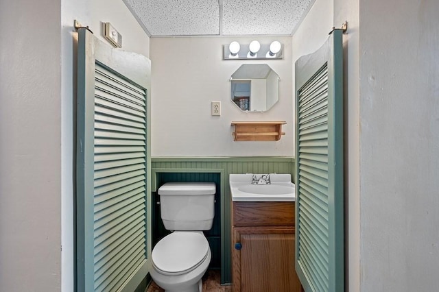 half bath with a wainscoted wall, vanity, and toilet