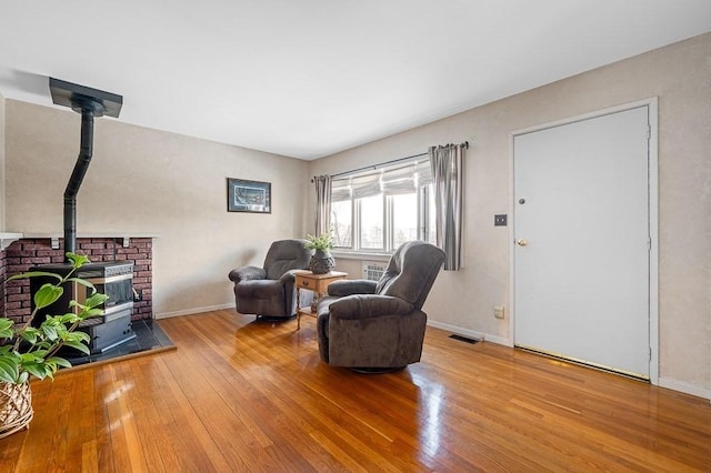 sitting room featuring a wood stove, baseboards, visible vents, and hardwood / wood-style floors