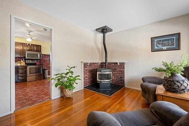 living room featuring a wood stove, a ceiling fan, baseboards, and hardwood / wood-style floors