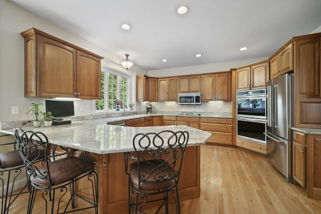 32 Bulkley Rd, Sudbury, MA 01776 - kitchen with appliances with stainless steel finishes, a peninsula, a kitchen bar, light stone countertops, and brown cabinets