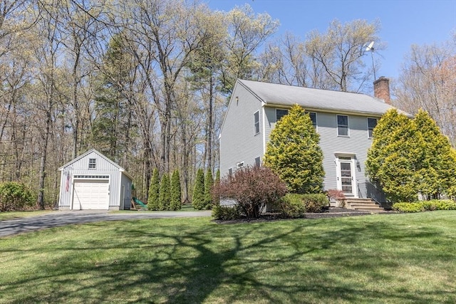 view of side of property with a detached garage, an outbuilding, a chimney, a yard, and driveway