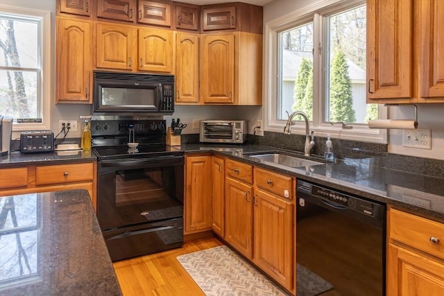 kitchen with a toaster, brown cabinets, a sink, light wood-style flooring, and black appliances